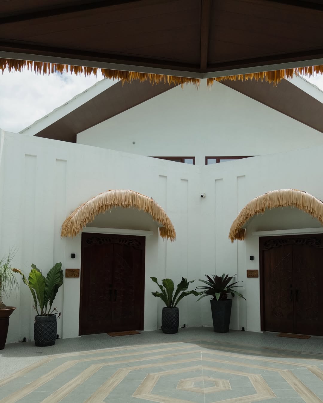 Ayatana entrance — white walls, thatched palm frond archways, and carved wood doors